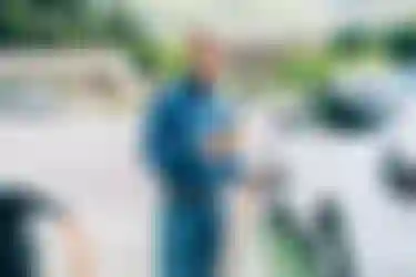 Ein Mann nutzt neben seinem an einer Ladesäule tankenden E-Auto stehend mit seinem Mobiltelefon die &Charge-App