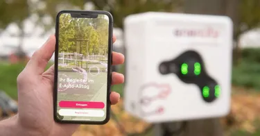 Eine Hand hält ein Smartphone, auf welchem die enercity easyGo-Ladeapp zu sehen ist. Im Hintergrund sieht man eine Ladestation für E-Autos.