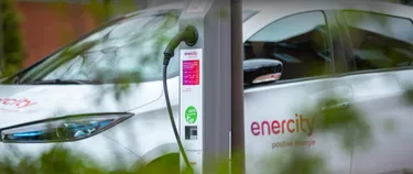 Das Bild zeigt eine Ladelaterne. Im Hintergrund steht ein E-Auto.