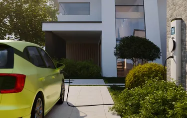 An electric car parked in front of a house entrance charges at a wallbox installed on a house wall