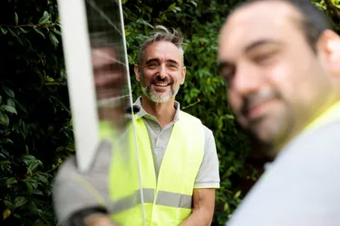 Zwei Männer mit gelben Schutzwesten transportieren eine Mini-Solaranlage durch einen Vorgarten.