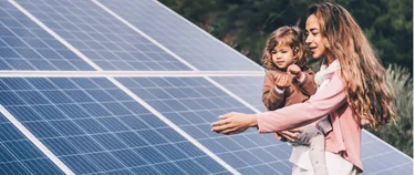 Eine Frau mit Kind auf dem Arm vor einem Solarmodul