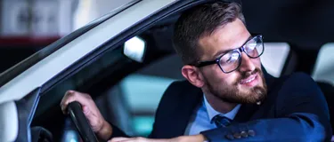 Mann mittleren Alters, der aus dem Fahrerfenster seines Autos nach hinten guckt.