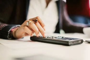 Nahaufnahme einer Frauenhand die auf einem Taschenrechner Zahlen eingibt