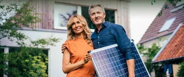 Ein Ehepaar steht im Garten und hält ein Solarpanel in den Händen.