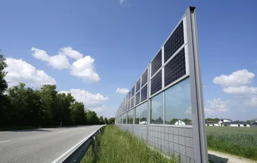 Am Rande einer Landstraße steht eine mit PV-Modulen ausgestattete Lärmschutzwand.