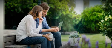 Wie klimafreundlich ist Smart Gardening? Das Bild zeigt eine Frau und einen Mann, die im Garten sitzen und gemeinsam auf ein Tablet schauen.
