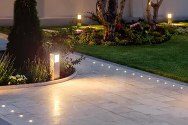 Smart lamps can be conveniently controlled via app or voice assistant. This picture shows a walkway in the garden with lighting spots in the ground as well as path lights at dusk.