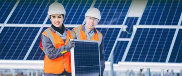 Zwei Menschen mit Warnweste und Sicherheitshelmen arbeiten am Aufbau einer PV-Anlage.