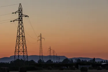 Eine Landschaft mit einer Reihe von Hochspannungsleitungsmasten im Abendrot.