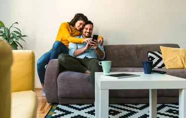 Eine Frau und ein Mann blicken auf dem Sofa sitzend auf das Display eines Smartphones