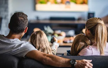 Eine vierköpfige Familie sitzt auf einem Sofa und schaut in Richtung ihres Fernsehers