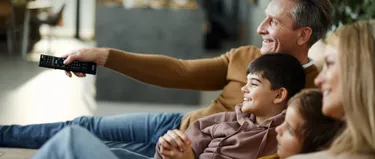 Eine vierköpfige Familie sitzt auf einem Sofa und schaut in Richtung ihres Fernsehers