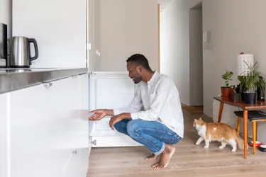: Das Bild zeigt einen jungen Mann, der vor seinem geöffneten Gefrierschrank in der Hocke sitzt und eine der Schubladen herauszieht.