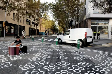 Ein Junge sitzt inmitten eines verkehrsberuhigten Platzes in Barcelona an einem kleinen Tisch und macht seine Hausaufgaben.