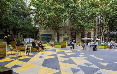 Verkehrsberuhigter Platz in Barcelona, auf dem Anwohner an Bänken und Tischen sitzen und sich unterhalten.