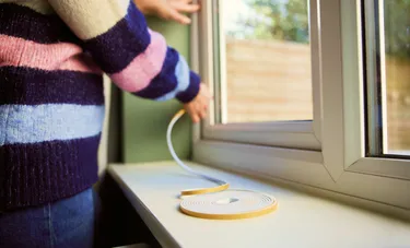 Nahaufnahme einer Person, die ein Fenster mit Dichtungsband abdichtet