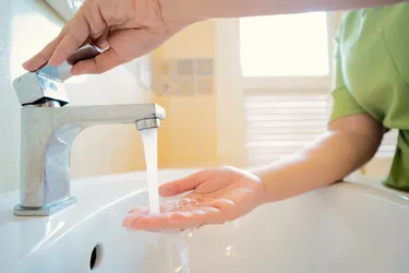 Nahaufnahme zweier Hände, die unter einem Wasserhahn in einem Badezimmer gewaschen werden