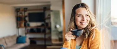 Eine Frau hält lächelnd eine Teetasse in der Hand.
