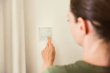 Eine Frau stellt an einem an einer Zimmerwand installierten Thermostat die Heizungstemperatur ein