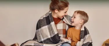 Eine Mutter und ihr Sohn kuscheln sich in eine Decke und schauen sich glücklich an.