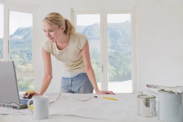 Junge Frau vor einem Schreibtisch mit Bauplänen und einen Laptop