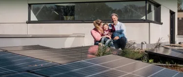 Eine Frau und ein Mann sitzen mit einem kleinen Mädchen zwischen Solarmodulen
