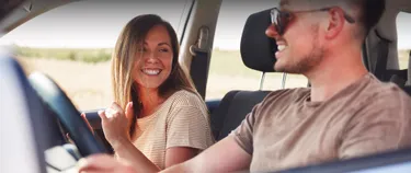 Ein Mann und eine Frau sitzen im Auto und sehen sich glücklich an.