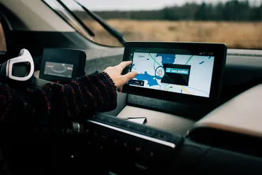 Blick in eine E-Autocockpit, in dem der Fahrer am Touchdisplay des Navigationssystems die nächstgelegene Ladesäule auswählt.