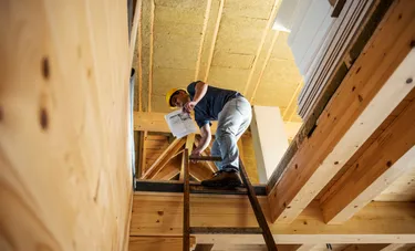 Ein Handwerker steht auf einer Leiter in einem Dachgeschoss das gedämmt wird