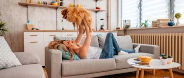 Frau liegt auf dem Sofa und hält einen Hund hoch.