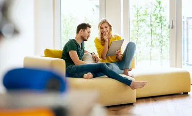 Ein auf einem Sofa sitzender Mann und eine Frau schauen gemeinsam auf den Bildschirm eines Laptops