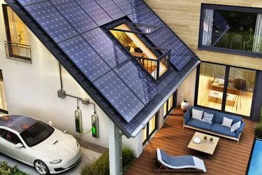 Das aus der Vogelperspektive fotografierte Bild zeigt ein modernes Haus mit PV-Anlage auf dem Dach und einer Wallbox an der Hauswand, an der ein E-Auto geladen wird.