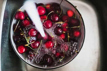 Eine Schüssel voller Kirschen wird unter dem Wasserhahn in der Spüle mit Wasser gefüllt.
