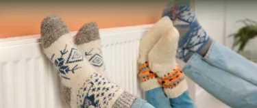 Drei Personen tragen Wollsocken und halten ihre Füße an die Heizung.